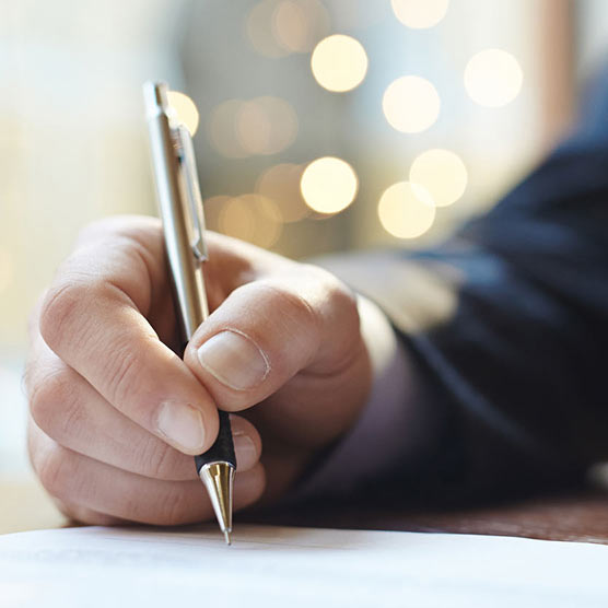 Photo d'une main qui tient un stylo dont la pointe est posée sur un papier