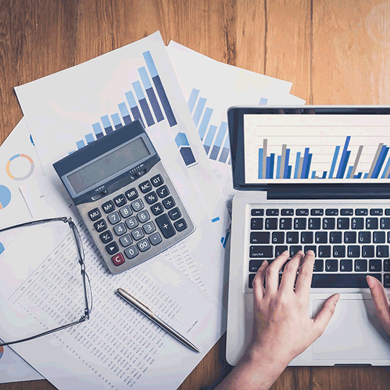 Photo en plongée d'un bureau où se trouve une calculatrice, un ordinateur portable et des feuilles remplies de graphiques et de chiffres
